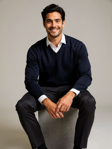 Man seated wearing navy V-neck wool blend jumper