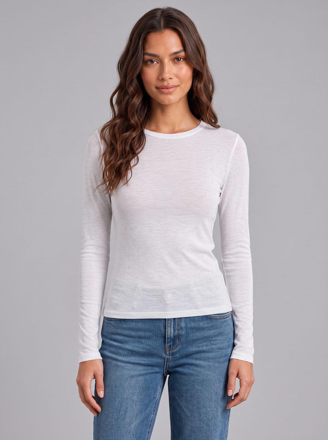 Woman wearing white slim fit round neck long sleeve top with blue jeans, front view