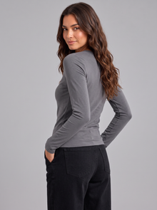 Woman wearing grey slim fit round neck long sleeve top with black trousers