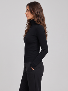 Woman wearing black ribbed roll neck long sleeve top with collar zip, side view