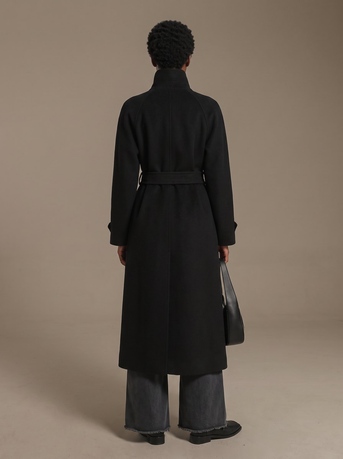 Woman wearing black belted longline wool coat with high stand collar and gold buttons, front view