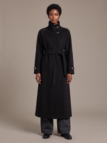 Woman wearing black belted longline wool coat with high stand collar and gold buttons, front view