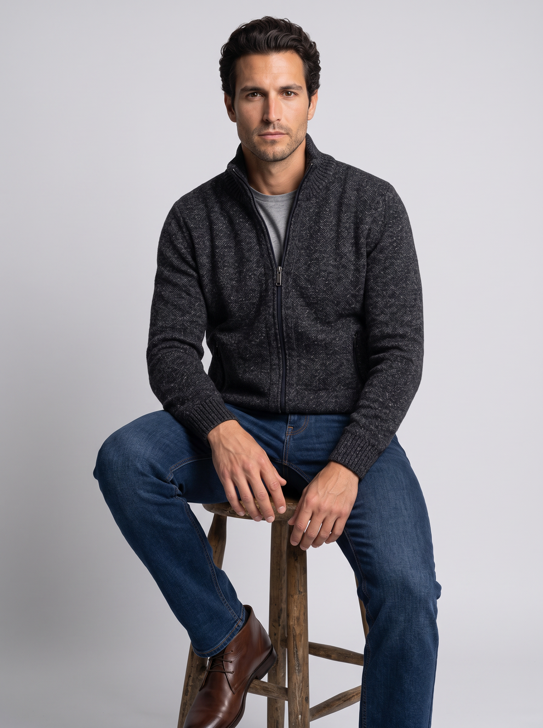 Man seated on stool in black merino wool full-zip cardigan