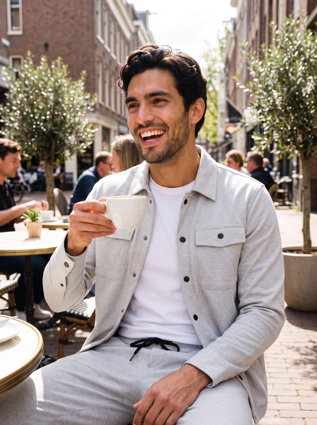 Man wearing light grey overshirt and trousers set at a cafe terrace