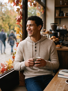 Man wearing sand beige cashmere hoodie in a cosy autumn coffee shop
