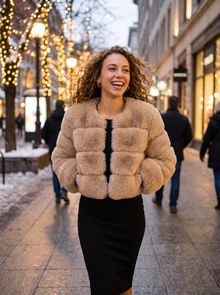 Woman wearing a cropped beige faux fur jacket on a winter evening street
