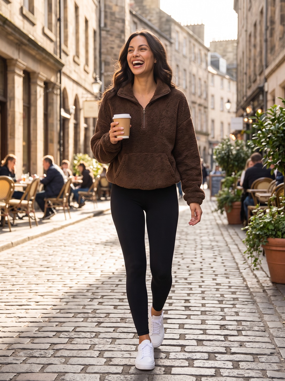 Woman walking in the city in brown fleece half-zip jumper holding a coffee