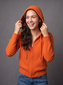 Woman laughing in orange knit zip hoodie cardigan with hood up