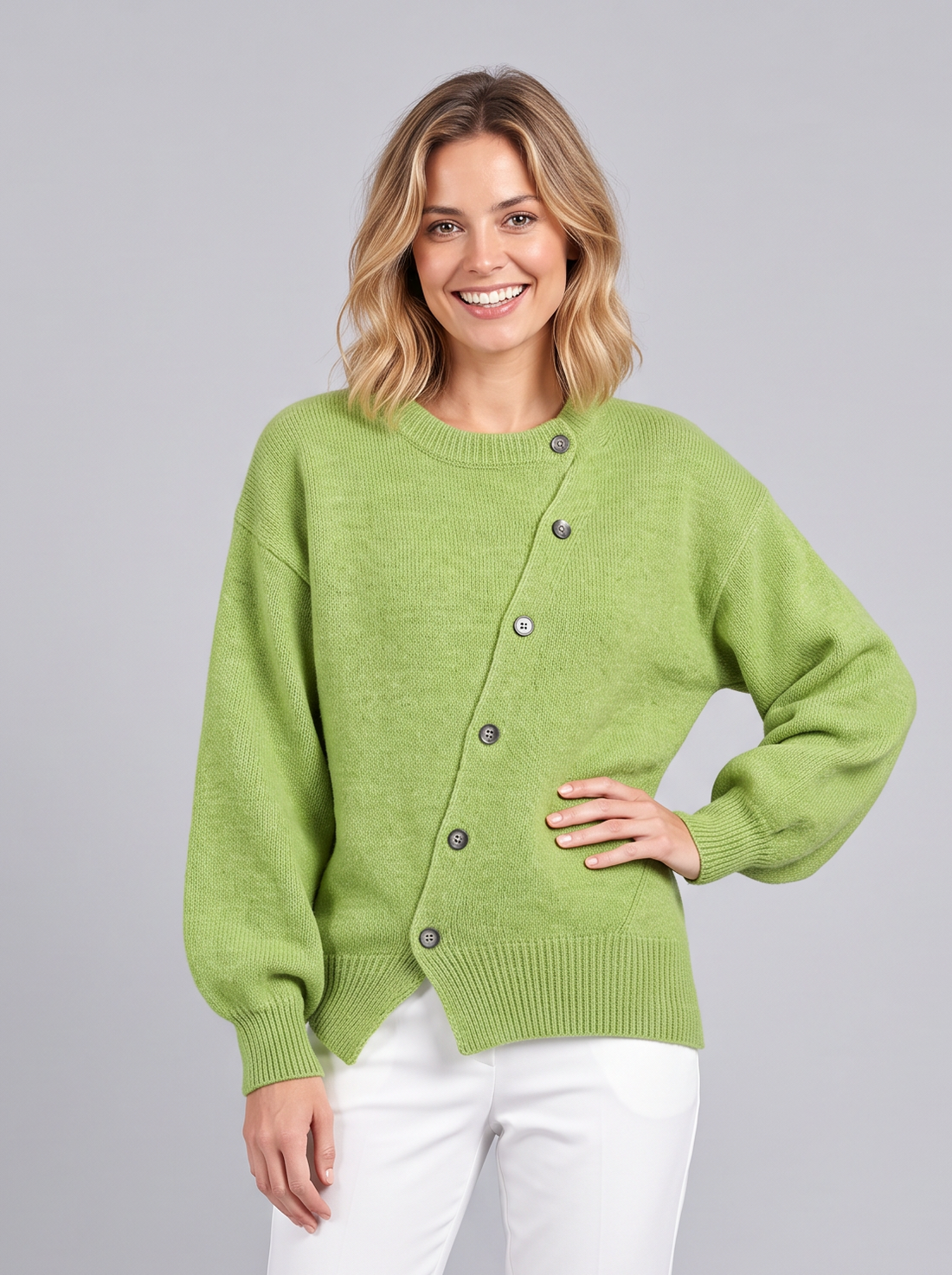 Woman wearing a green cashmere knit jumper with asymmetric button front and white trousers