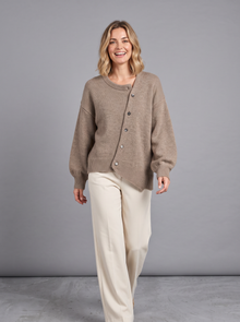 Woman walking in a brown cashmere button-front jumper with cream wide-leg trousers