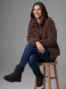 Woman seated in a dark brown teddy fleece jacket and black snow boots