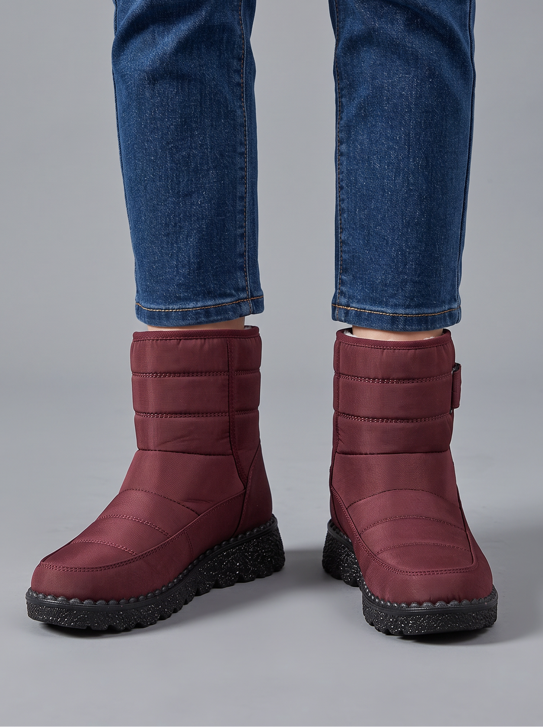 Burgundy quilted snow boots with velcro strap worn with jeans, front view