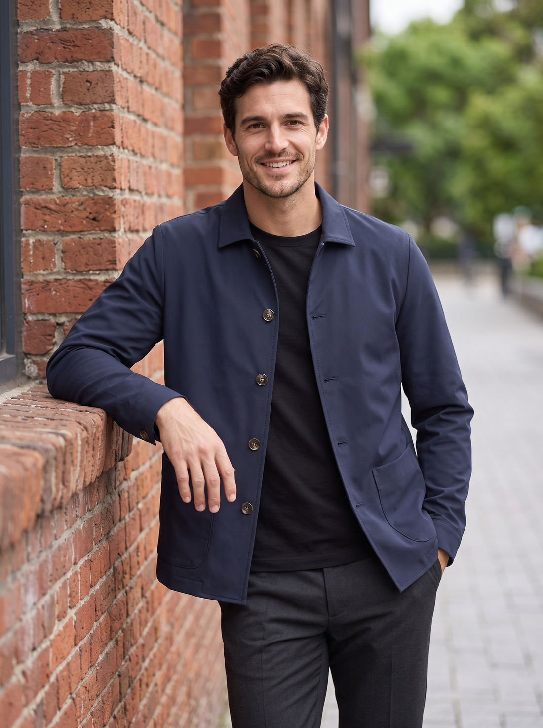 Man leaning on a brick wall wearing a navy button-up shirt jacket