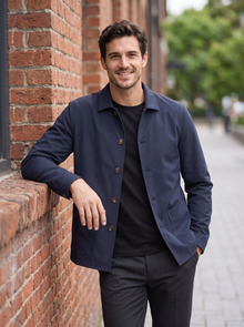 Man leaning on a brick wall wearing a navy button-up shirt jacket