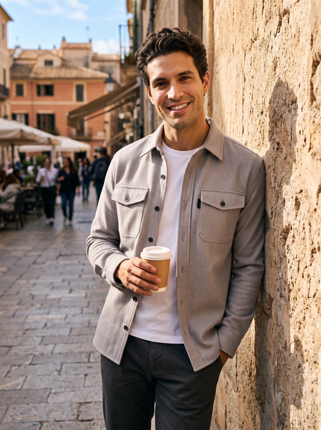 Man leaning on a sunlit wall wearing a light grey overshirt